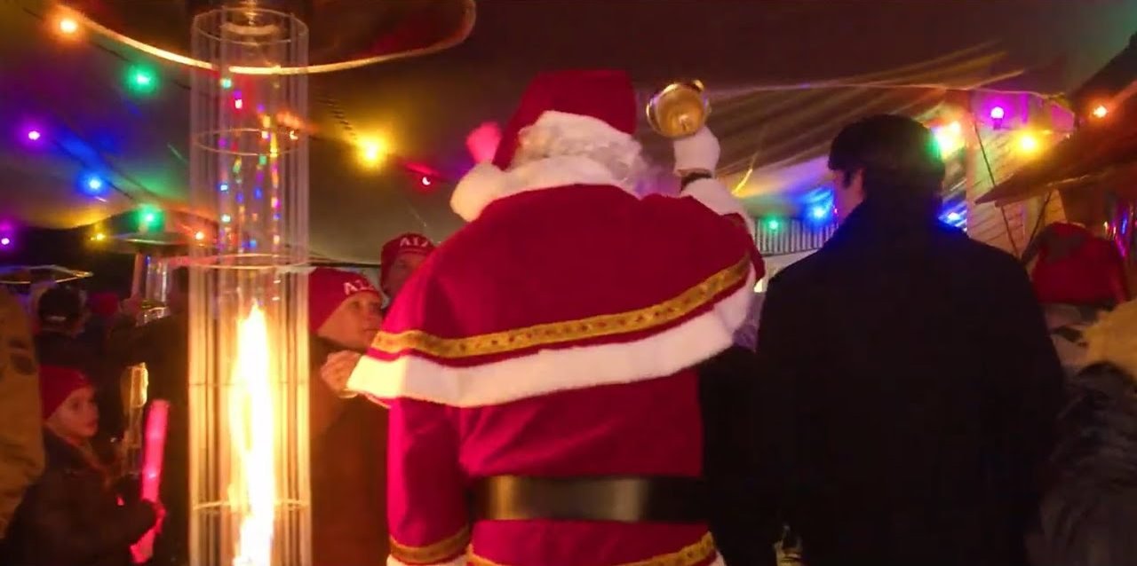 De kerstman tussen de gasten in een tent met gekleurde lichtjes